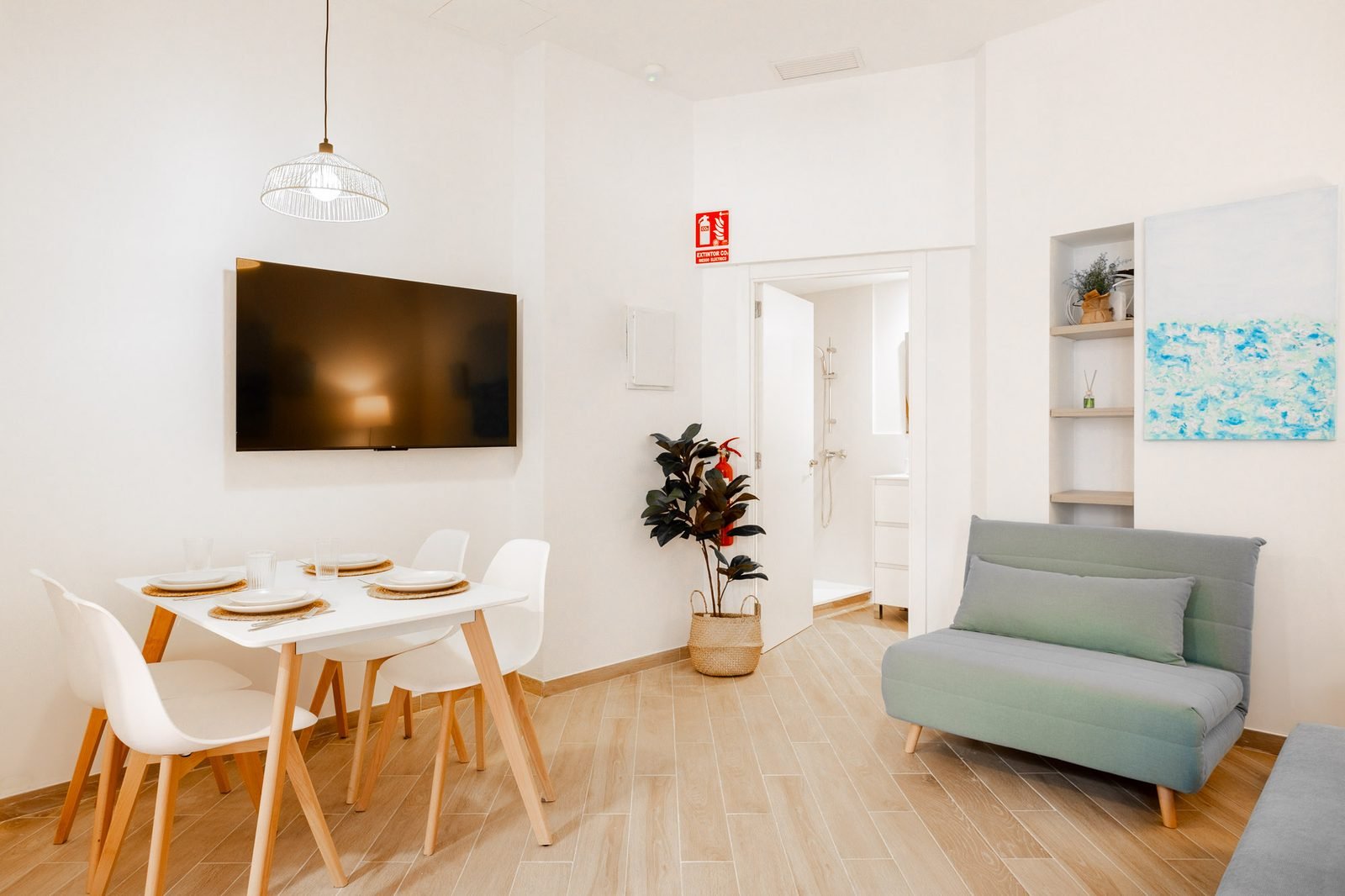 Zona de estar con mesa de comedor, televisor de pared y acceso al baño