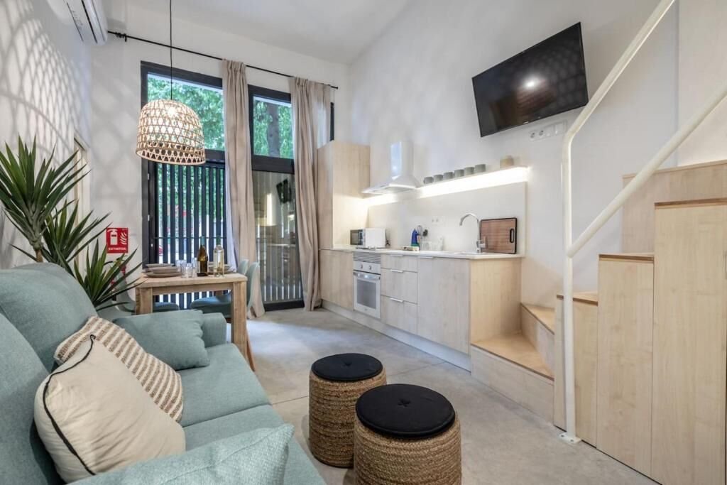Salón con sofá, mesa de comedor, cocina y escalera de acceso al altillo