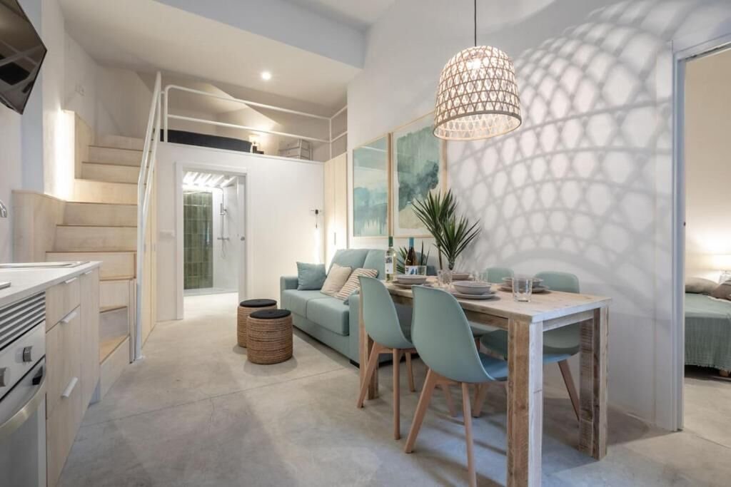 Salón con mesa de comedor de madera, sillas y altillo visible al fondo